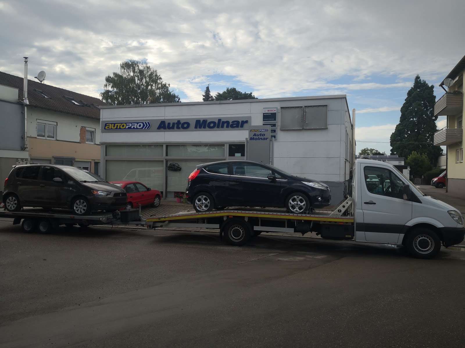 Abschleppfahrzeug mit Fahrzeugen vor dem Werkstattgebäude
